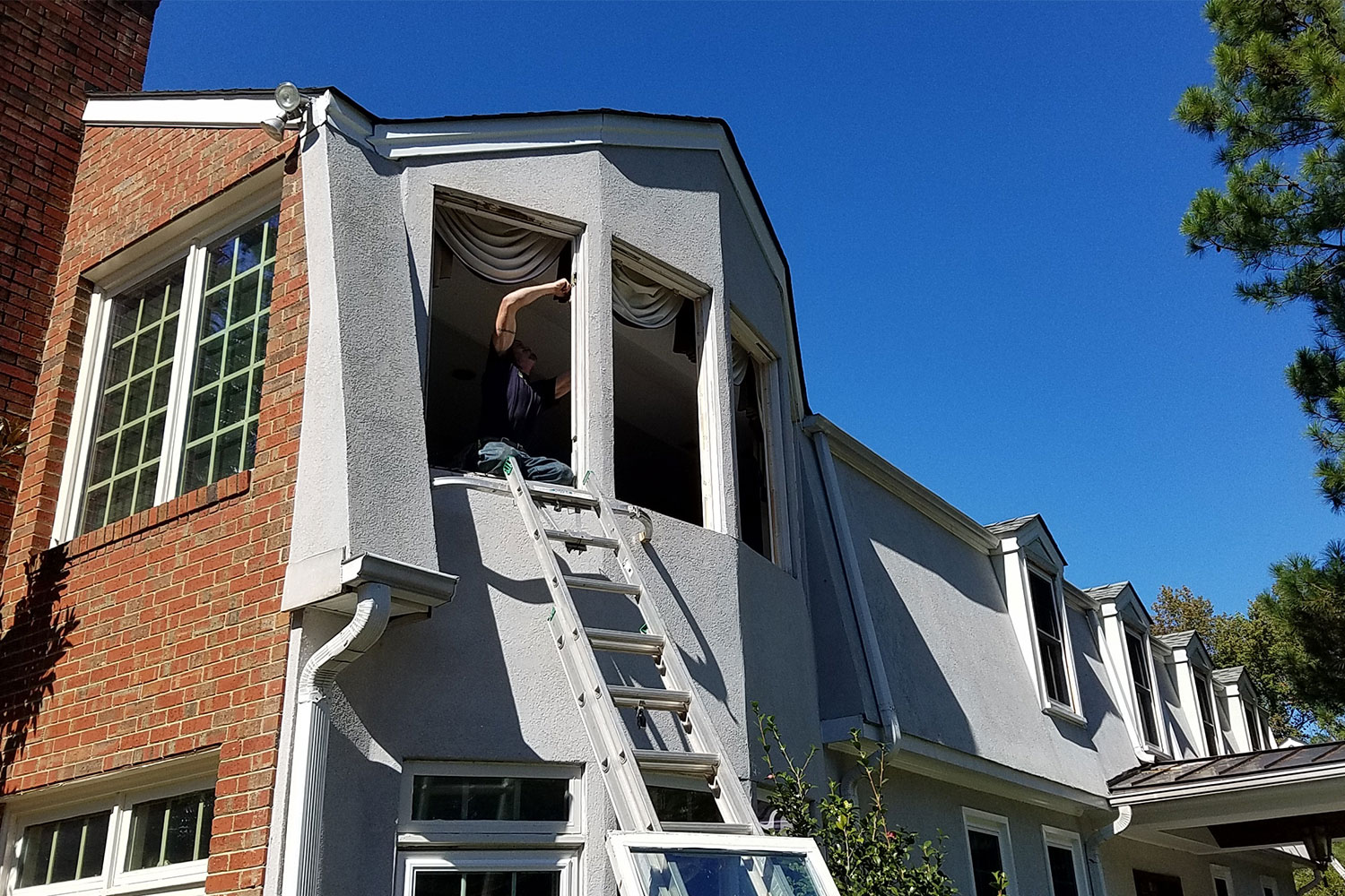 A man working on the windows of a gray house