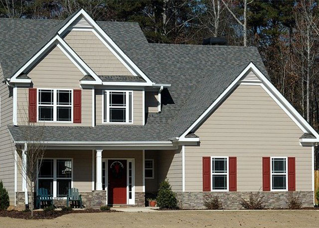 A house with grayish paint and red details in windows and the door